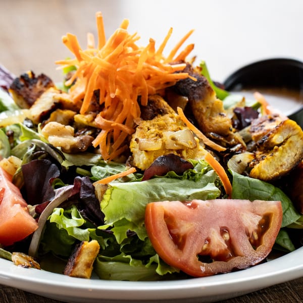 A fresh salad with mixed greens, grilled chicken, shredded carrots, and sliced tomatoes.