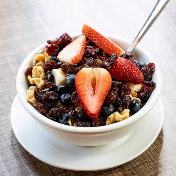 A white bowl of Village Coffee's oatmeal with strawberries, blueberries, raisins, and walnuts.