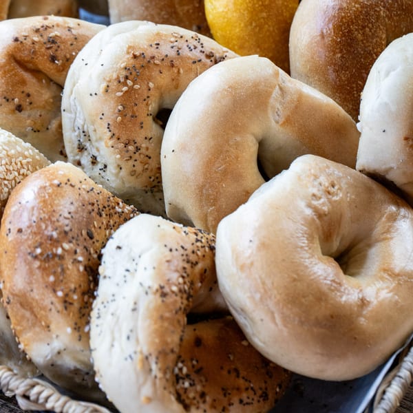 A basket filled with various fresh bagels, some plain, some with sesame and poppy seeds.