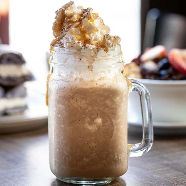 A Village Coffee blended coffee drink in a mason jar, topped with whipped cream and caramel drizzle.