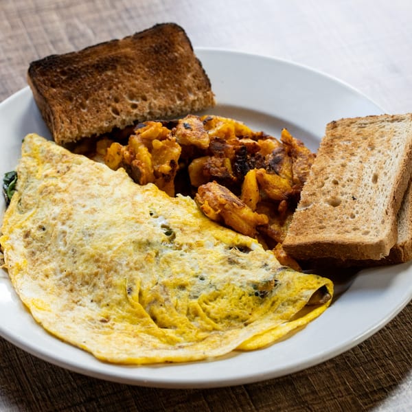 A Village Coffee breakfast plate with a fluffy omelet, crispy home fries, and two slices of toast.