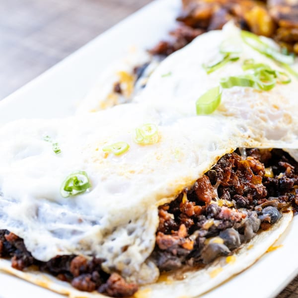 Breakfast tacos with fried eggs, black beans, chorizo, and green onions on a white plate.