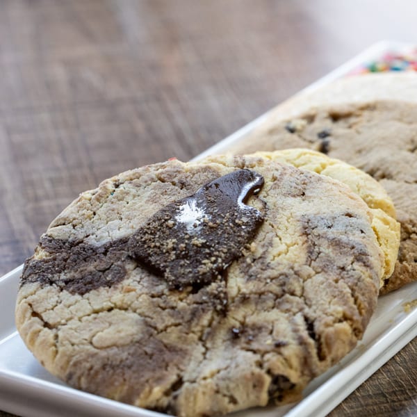Close-up of three marbled cookies with chocolate chunks on a white rectangular plate.