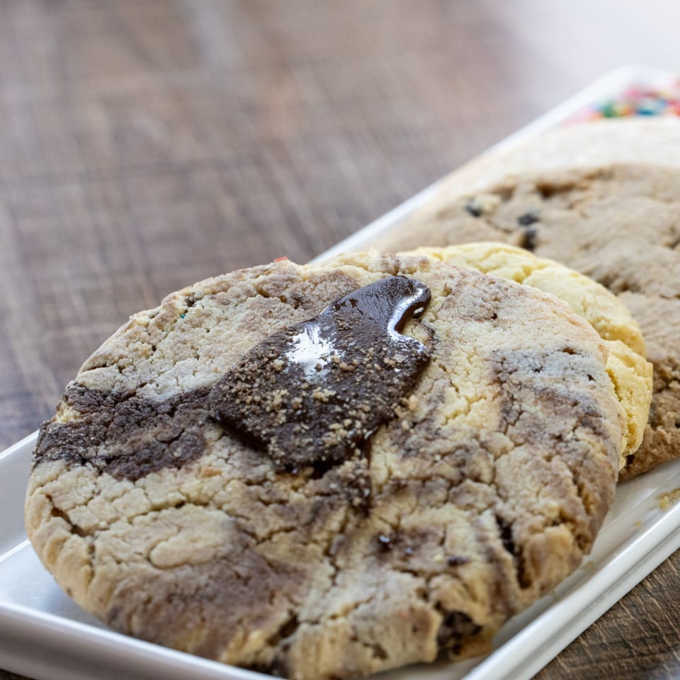 Close-up of three marbled cookies with chocolate chunks on a white rectangular plate.